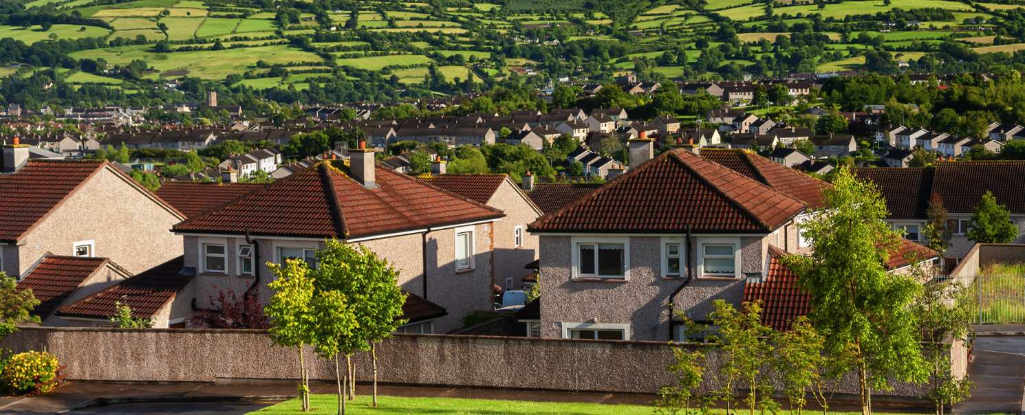 Íomhá de thithe in eastát sa tulra agus cnoic agus tuath sa chúlra